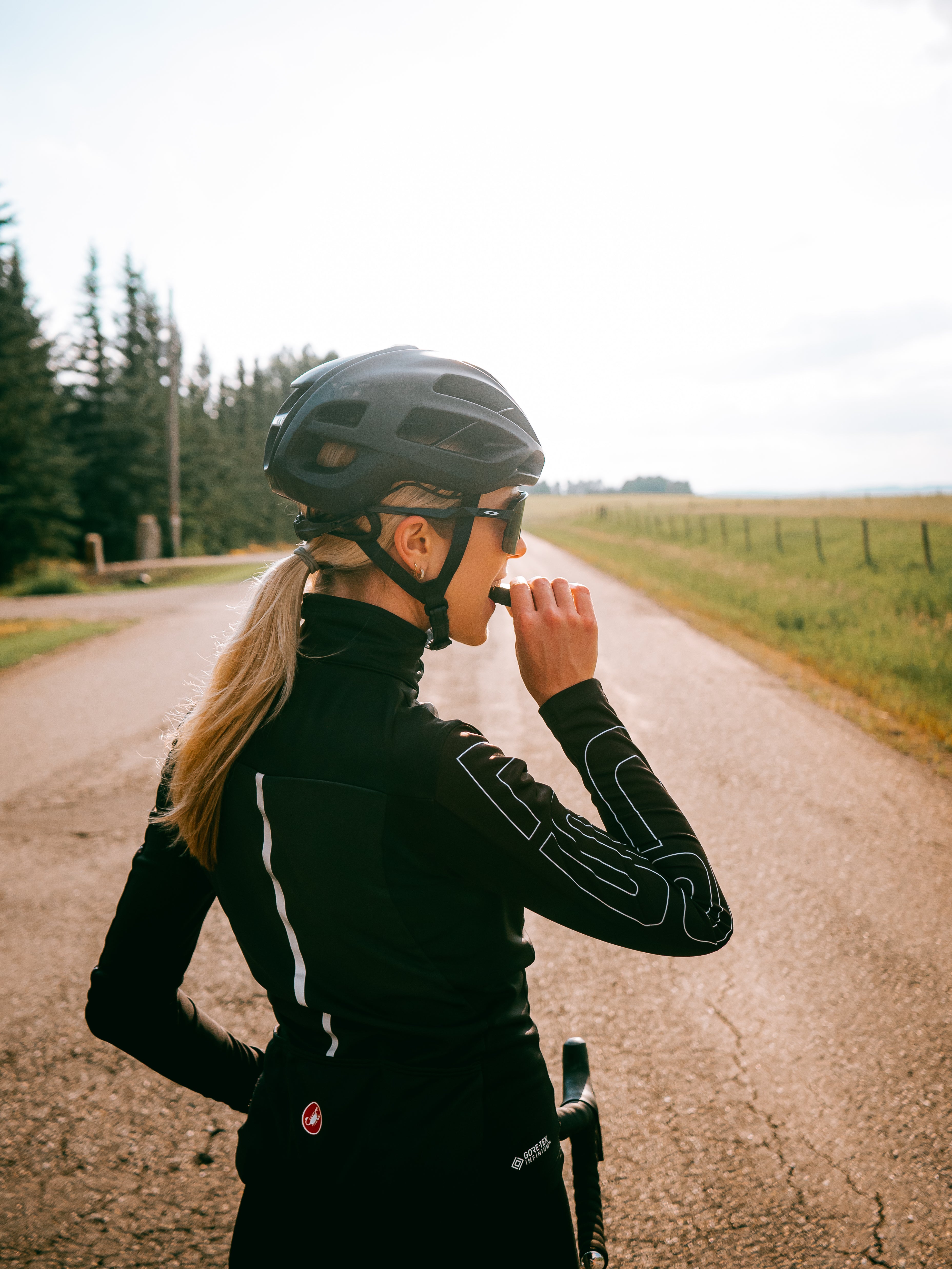 Blond girl in a helmet and black biking gear eating an Algi IMPACT Bar